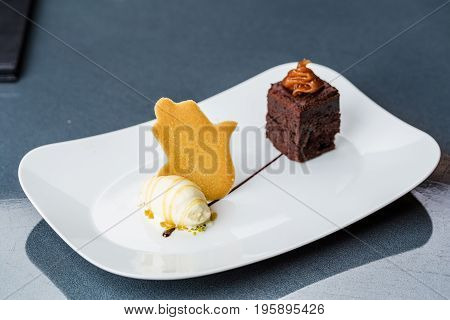 One scoop of the ice cream served on the white plate with brownie and buscuit
