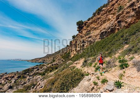 Man running in inspirational mountains at seaside. Young athlete male training and doing workout outdoors in nature. Sport and fitness training inspiration and motivation.