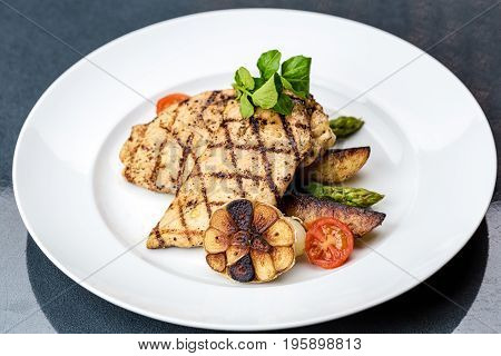 Grilled chicken fillet served with french fries, asparagus and cherry tomatoes, decorated with grilled garlic and baby spinach