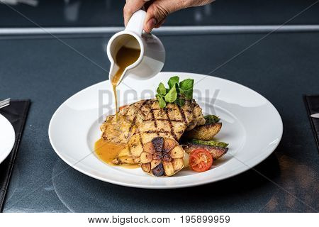 Grilled chicken fillet served with french fries, asparagus and cherry tomatoes, decorated with grilled garlic and baby spinach