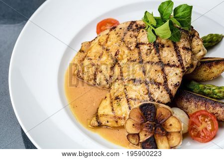 Grilled chicken fillet served with french fries, asparagus and cherry tomatoes, decorated with grilled garlic and baby spinach