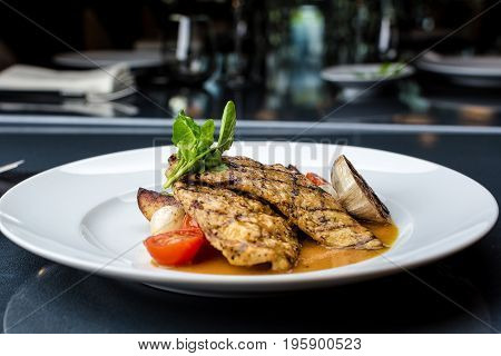 Grilled chicken fillet served with french fries, asparagus and cherry tomatoes, decorated with grilled garlic and baby spinach