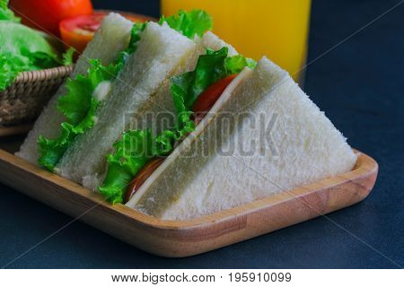 Triangle slice piece of sandwich ham cheese with lettuce and tomato on wood plate. Homemade sandwich served with orange juice for breakfast or lunch. Delicious ham cheese sandwich ready to served on granite table with fresh orange juice