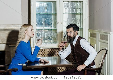 Boyfriend and girlfriend drinking red wine in restaurant. Woman or girl and man or hipster sitting with martini glasses at table. Couple in love. Date dating. Alcohol appetizer. Addictive convive