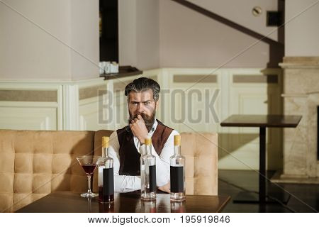 Hipster Sitting On Sofa With Martini Glass And Three Bottles