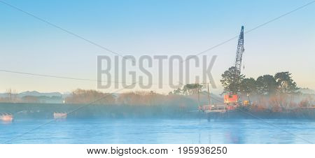 Early morning mist around a bridge building crane on the Manawatu river.