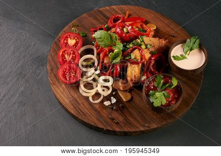 Close-up of grilled spicy chicken breast with fresh baked vegetables and branded garlic sauce on a black stone background. Healthy low-calories food.