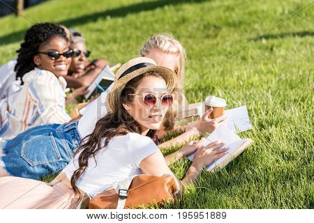 mutiethnic students lying on green grass while studying in park