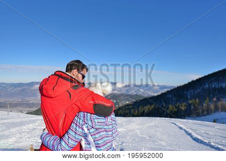 Rear view of a loving couple in fur hood jackets looking at snowed mountain range.