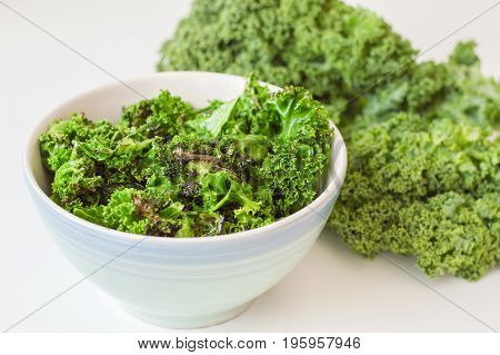 Kale salad in blue bowl and fresh kale leaves on white table. Kale chips mixed with fresh leaves. Vegetarian food. Healthy eating