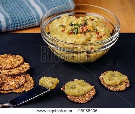 Enjoy roasted garlic on whole grain crackers. Food is on a black board with a butter knife and blue napkin.