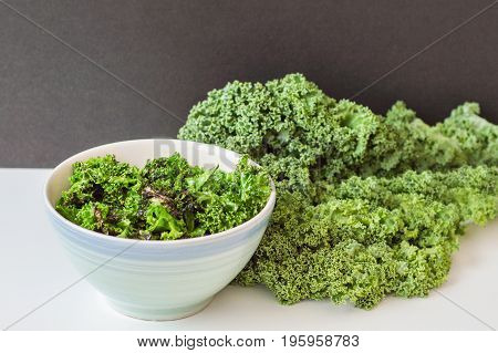 Bowl with crispy kale chips and fresh kale bunch on white table. Kale salad