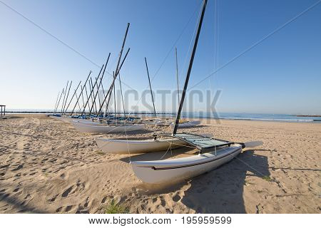 group of catamaran boats in row on the beach Els Terrers in Benicassim Castellon Valencia Spain Europe. Blue clear sky and Mediterranean Sea