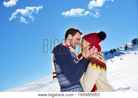 Loving couple embracing in winter park. They put colored caps and scarves