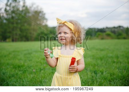 Little kid with happy smile holding little tube and device for blowing bubbles standing in meadow.