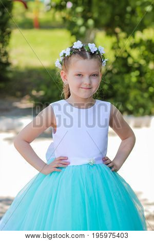 Cute Small Girl Dressed In Blue And White Dress With A Wreath Of Artificial Flowers On Her Head, Chi