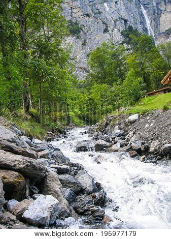 Mountain River Or Creek With Staubbach Watterfall In Background In Interlaken, Switzerland During Su