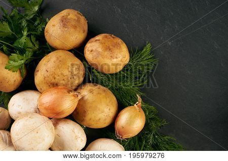 Raw fresh onions potatoes garlic mushroom greens and seasoning on dark stone background with copy space. Top view ingredients for cooking a delicious cream soup. Healthy vegetarian food.