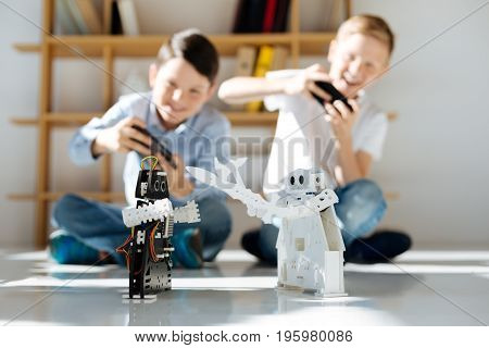 Quality time. Two happy pre-teen boys sitting on the floor and controlling two cosmic warrior robots fighting with each other