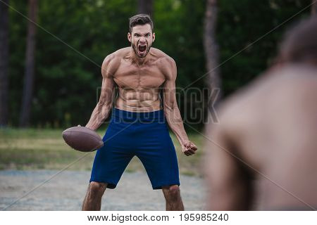 young handsome male football player yelling and holding ball on court
