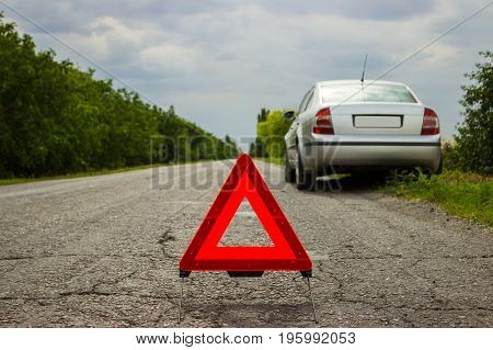Red triangle of a car on the road. Car warning triangle on the road against the city in the evening. Breakdown of the car in bad weather.