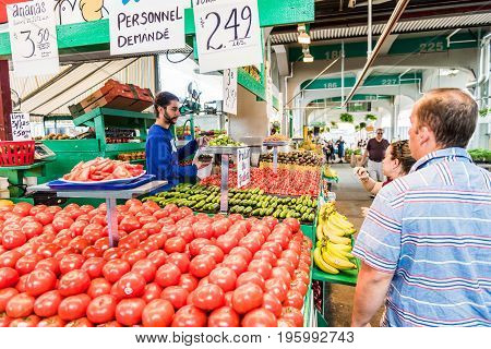 Montreal Canada - May 27 2017: Man buying produce by tomato stand with sample slices at Jean-Talon farmers market with fruit displays