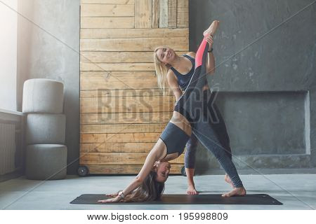 Yoga teacher and beginner in class, making asana exercises. Young woman making one-legged downward-facing dog pose. Healthy lifestyle in fitness club. Stretching with coach