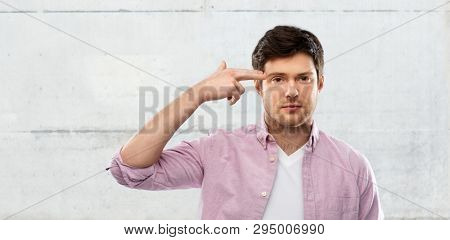 negative emotion, expression and stress concept - bored young man shooting himself to head by finger gun gesture over grey concrete wall background