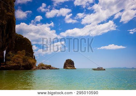 The Rock In The Sea Is Painted With Gold Paint. Speedboat Floats Nearby. Blue Sky, A Lot Of Clouds. 