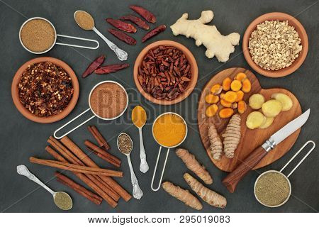 Fat busting spices for losing weight concept with fresh and dried turmeric, ginger, cumin, chilli, cinnamon and gymnema sylvestre used to suppress appetite. Top view on slate background.
