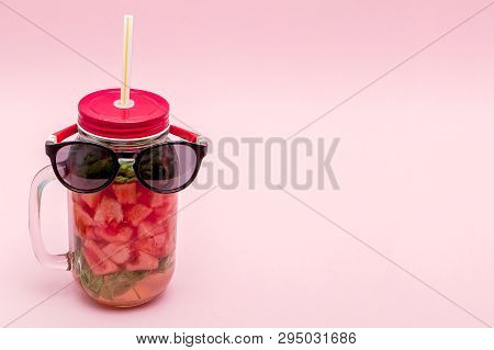 Glasses Lying On A Jar Of Cold Fresh Lemonade With Piece Of Watermelon And Ice On Pink Background
