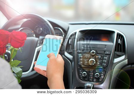 A Young Man Holding A Smartphone, Inside The Car, With A Color Screen For Text, Flowers Waiting For 