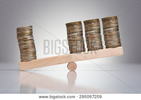 Stack Of Coins On Wooden Seesaw Over Gray Background