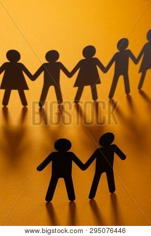 Black paper figure of male couple in front of a crowd of paper people holding hands on orange surface. Social movement, protest, minorities concept.