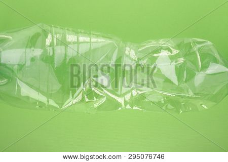 Squashed plastic bottle on vivid green background. Plastic utilisation concept. Ecological problem, global environment.