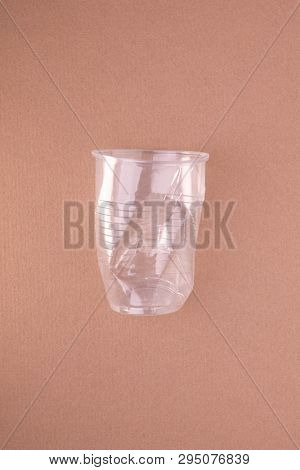 Squashed plastic cup on beige tan green background. Plastic utilisation concept. Ecological problem, global environment.