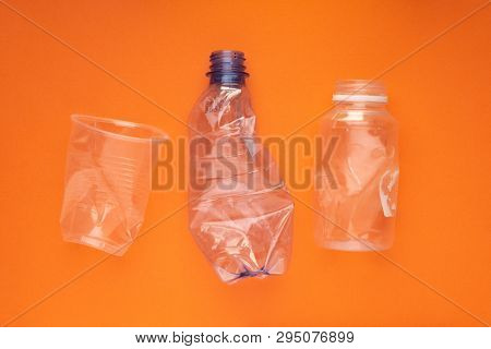 Squashed plastic bottles and a cup on orange background. Plastic utilisation concept. Ecological problem, global environment.