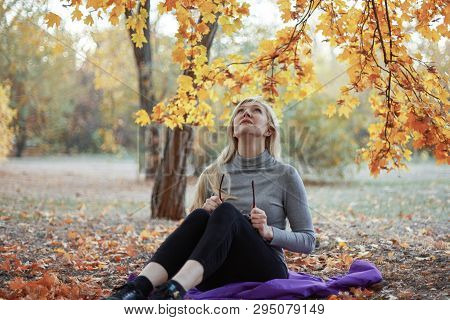 Middle Aged Caucasian Woman Sits Alone At Golden Autumn Park With Tablet, Smiling. Casual Wear, Glas