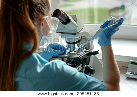 Woman Laborant Working With Microscope Holding Automatic Pipette