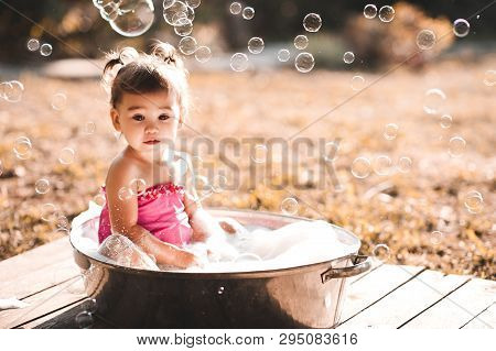 Cute Baby Girl 1-2 Year Old Having Bath With Soap Bubbles Outdoors Close Up. Summer Time. Childhood.