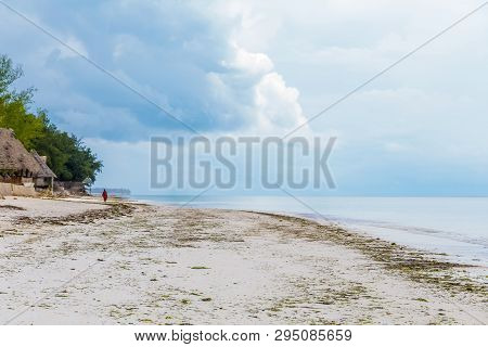 Deserted Ocean Beach With A Lonely Figure In The Distance. Blue Water And Blue Sky, No Clouds.