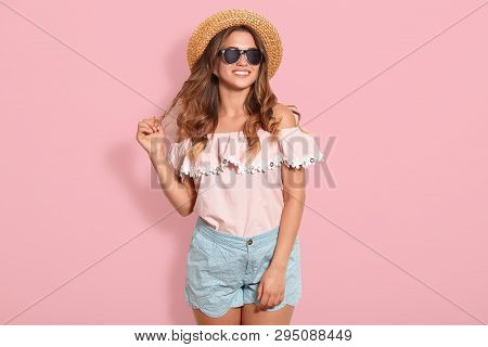 Beautiful Young Woman In Rose Summer Blouse, Blue Short, Sunglasses And Sun Hat, Pulling Her Hair As