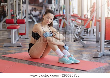 Image Of Relaxed Fitness Woman With Perfect Figure Sits On Exercise Mat, Looking Thoughtfully Down, 