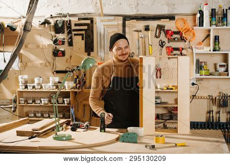Portrait Of Working Handsome Middle Aged Bearded Carpenter In A Watch Cap. He Is Making Furniture On
