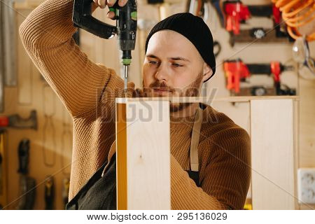 Portrait Of Working Handsome Middle Aged Bearded Carpenter In A Watch Cap. He Is Making Furniture On