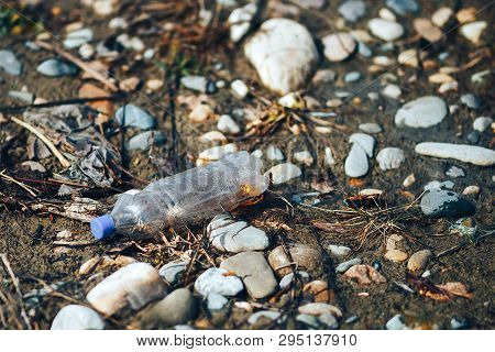 Environmental Pollution Plastic Bottle With Blue Lid Brown Liquid Inside On The Beach Among Stones A