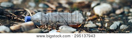 Environmental Pollution Plastic Bottle With Blue Lid Brown Liquid Inside On The Beach Among Stones A