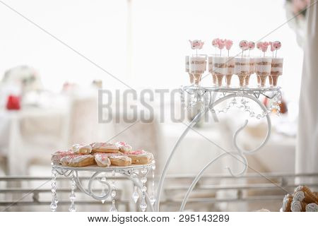 On A Bright Blurry Background Are The Cakes On A Beautiful Stand. Nearby Are Cups Of Desserts On A D