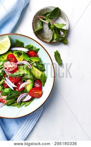 Mixed salad made with cherry tomatoes, arugula, red onion, avocado and mint leaves. Healthy home made food. Flat lay. Copy space