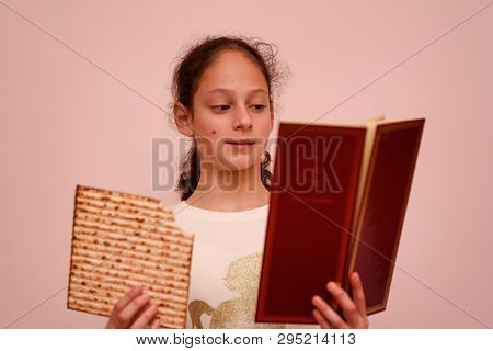Portrait Of The Cute Teenager Girl Holding Matzah And Reads The Passover Haggadah. Jewish Child Eati